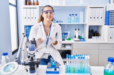 Laboratuvarda çalışan Latin asıllı genç bir kadın tiksindirici tepki verdiği için mutsuz ve korkmuş bir ifade takınıyor. Eller havada. 