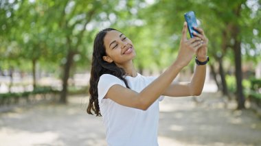 Afro-Amerikalı kadın, parkta akıllı telefonun yanında kendinden emin bir şekilde selfie çekiyor.