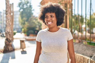 Afro-Amerikalı kadın gülümsüyor. Kendinden emin bir şekilde caddeye bakıyor.