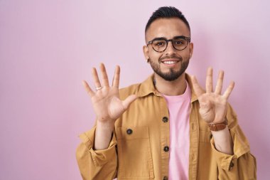 Young hispanic man standing over pink background showing and pointing up with fingers number nine while smiling confident and happy. 