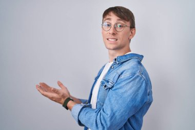 Beyaz, sarışın, gözlüklü, elleri açık, fotokopi alanı gösteren, gülümseyen, mutlu, mutlu bir gülümseme sunan bir adam. 