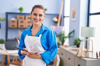 Young woman artist holding paintbrush and palette at art studio