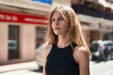 Sokakta ciddi bir ifadeyle yan tarafa bakan genç sarışın kadın.