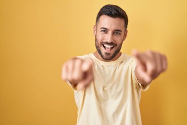 Sarı arka planda dikilen yakışıklı İspanyol adam seni ve kamerayı işaret ediyor, gülümsüyor olumlu ve neşeli. 