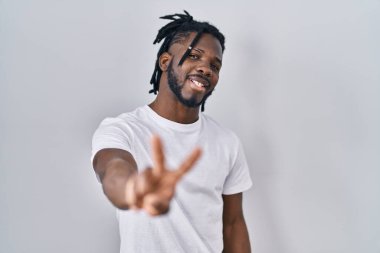 Beyaz arka planda kazaklı Afrikalı bir adam kameraya bakıp zafer işareti yaparken gülümsüyor. İki numara.. 