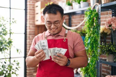 Young chinese man florist smiling confident counting dollars at florist