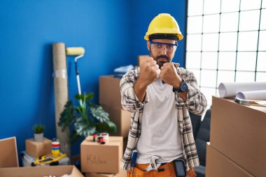 Sakallı genç İspanyol bir adam ev tadilatında çalışıyor. Yumruk savunma hareketleriyle dövüşmeye hazır. Kızgın ve üzgün. 