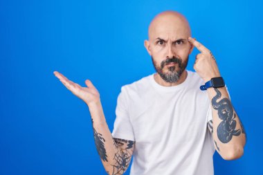Mavi arka planda dikilen İspanyol dövmeli adam avuç içi açık fotokopi alanı ve alnını göstermekten rahatsız ve kafası karışık. Bunu bir düşün.. 