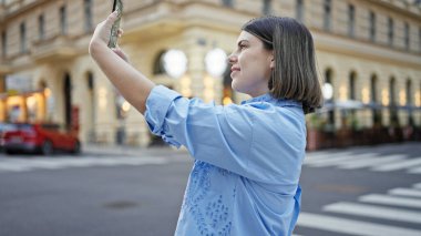 Genç ve güzel İspanyol kadın Viyana sokaklarında akıllı telefonuyla selfie çekiyor.