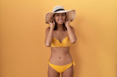 Genç İspanyol kadın bikini ve yaz şapkası takıyor. Yüksek sesli müzik sesi için kulaklarını parmaklarıyla kapatıyor. sağır kavramı. 