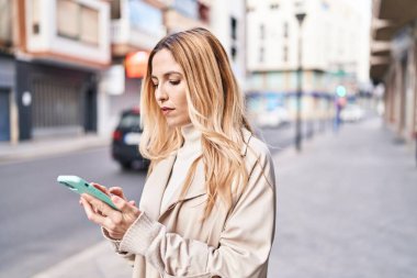 Sokakta akıllı telefon kullanan genç sarışın kadın.