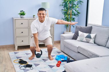 Genç Latin adam evde kettlebell kullanarak bacak egzersizi yapıyor.