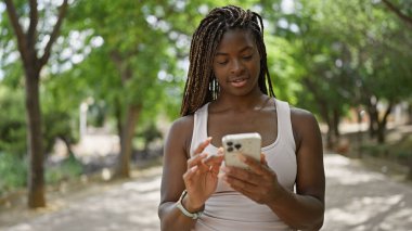 Parkta gülümseyen akıllı telefon kullanan Afrikalı Amerikalı kadın.