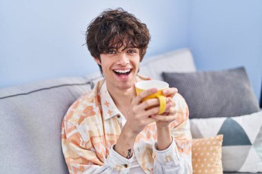 Genç İspanyol adam evdeki kanepede kahve içiyor.