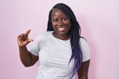 Pembe arka planda duran Afrikalı genç bir kadın gülümsüyor ve el hareketleriyle hareket ediyor parmaklarıyla işaret veriyor ve kameraya bakıyor. ölçüm kavramı. 