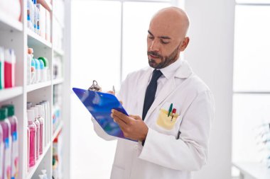 Young bald man pharmacist writing on document at pharmacy