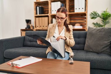 Psikoloji kliniğinde genç beyaz kadın psikolog elinde klasörle ilgili belgeler tutuyor.