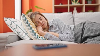 Young blonde woman lying on sofa sleeping at home