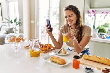 Genç ve güzel İspanyol kadın kahvaltısını mutfakta akıllı telefon kullanarak yapıyor.