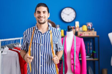 Young hispanic man tailor smiling confident standing at sewing studio