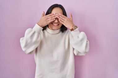 Pembe arka planda duran genç Güney Asyalı kadın elleri gülücüklü ve komik bir şekilde gözlerini kapatıyor. kör kavram. 