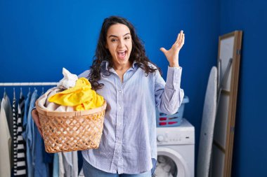 Çamaşır sepetini tutan genç esmer kadın zaferi mutlu bir gülümsemeyle ve kazanan yüz ifadesiyle kutluyor. 