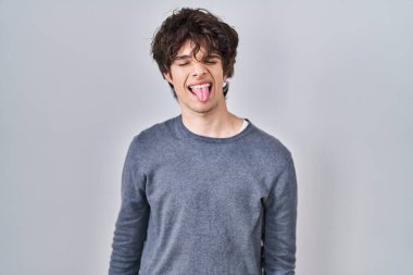 Young man standing over isolated background sticking tongue out happy with funny expression. emotion concept. 