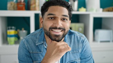 Afro-Amerikalı bir adam yemek masasında kendinden emin bir şekilde oturuyor.