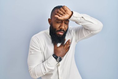 Afro-Amerikalı adam mavi arka planda duruyor. Hastalık, ateş, grip ve virüs için alnına dokunuyor. 