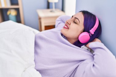 Genç, güzel, iri yarı bir kadın yatak odasında uzanmış müzik dinliyor.