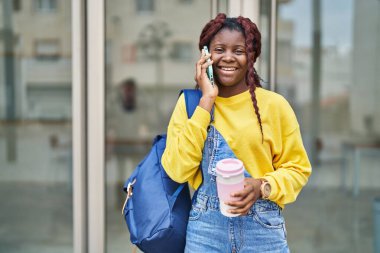 African american woman student talking on smartphone drinking coffee at university