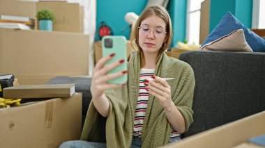 Genç sarışın kadın yeni evinde termometre gösteriyor.