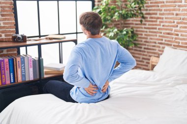 Young caucasian man suffering for back injury sitting on bed at bedroom