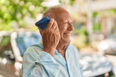 Senior grey-haired man smiling confident listening audio message by the smartphone at street