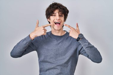 Young man standing over isolated background smiling cheerful showing and pointing with fingers teeth and mouth. dental health concept. 