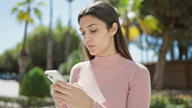 Genç, güzel, İspanyol bir kadın parkta akıllı telefon kullanıyor.