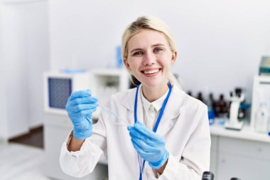 Genç sarışın bilim adamı laboratuarda numuneye sıvı döküyor.