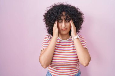 Orta Doğu 'lu genç bir kadın pembe arka planda, eli başının üstünde duruyor. Stres yüzünden başı ağrıyor. migren ağrısı. 