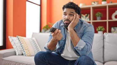 Afro-Amerikalı bir adam televizyon seyrediyor. Evde sıkıcı bir ifadeyle oturuyor.