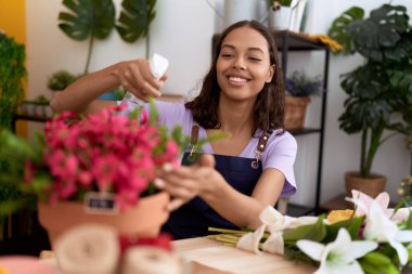 Young african american woman florist using diffuser watering plant at flower shop