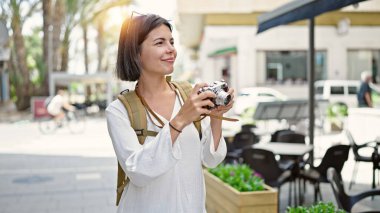 Genç, güzel İspanyol kadın turist kahve dükkanının terasında eski model kamera kullanarak gülümsüyor.