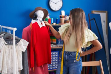 Young beautiful hispanic woman tailor holding t shirt at clothing factory