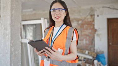 İnşaat alanında dokunmatik ped kullanarak gülümseyen genç Çinli kadın inşaatçı.