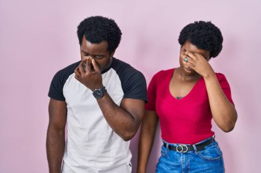 Genç Afro-Amerikan çift pembe arka planda dikiliyor yorgun burunlarını ve gözlerini ovuşturup yorgunluk ve baş ağrısı hissediyorlar. Stres ve hüsran kavramı. 