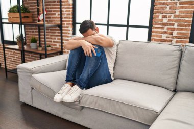 Young hispanic man stressed sitting on sofa at home