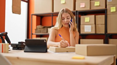 Genç sarışın kadın ecommerce iş işçisi. Ofiste paket üzerinde akıllı telefon yazısıyla konuşuyor.