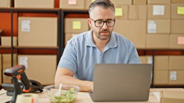 Ofisteki masada dizüstü bilgisayarla oturan gri saçlı adam ekomünikasyon işi.