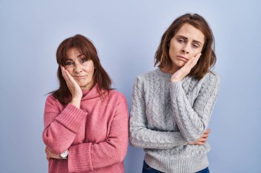 Mother and daughter standing over blue background thinking looking tired and bored with depression problems with crossed arms.  clipart