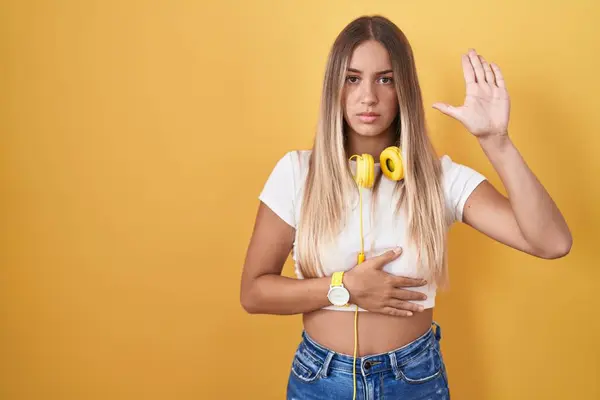Young Blonde Woman Standing Yellow Background Wearing Headphones Swearing Hand — Stock Photo, Image