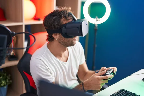 Young hispanic man streamer playing video game using virtual reality glasses and joystick at music studio